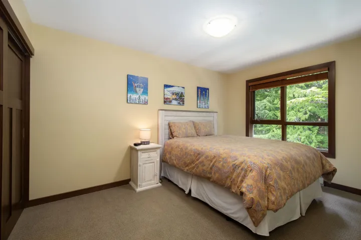 Carpeted bedroom featuring a large window with a wooded backdrop, a built-in closet with sliding wood doors, and baseboard trim