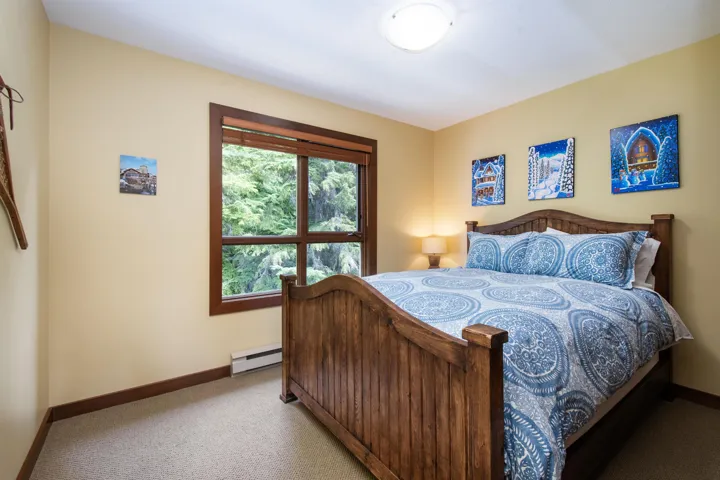 Bedroom featuring a large multi-pane window with wood trim, wall-to-wall carpeting, light-colored walls, and a ceiling-mounted light fixture