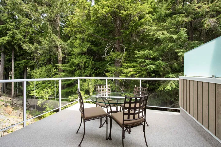 Spacious balcony featuring a textured gray surface, glass panel railings, and a privacy wall with vertical wood paneling and a frosted glass top