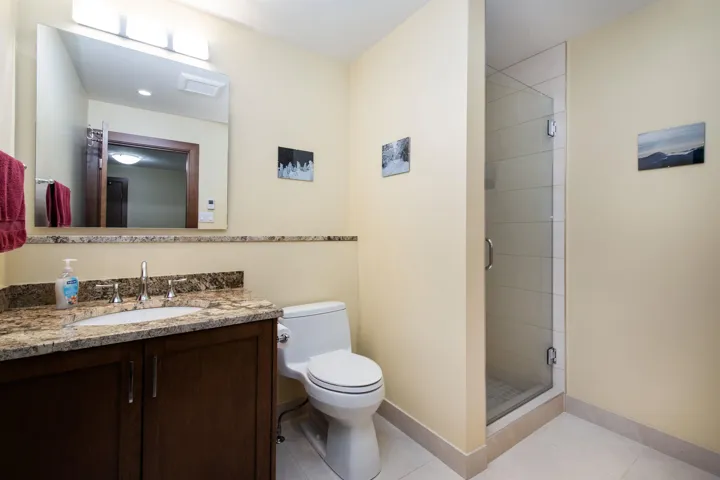 Bathroom featuring a wood-finish vanity with a granite countertop and undermount sink, a frameless glass shower enclosure, and light-toned tile flooring