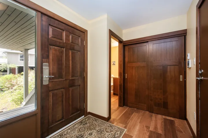 Entryway featuring a rich wood-finish front door with a sidelight, wood-finish flooring, and a pair of wood-finish sliding closet doors