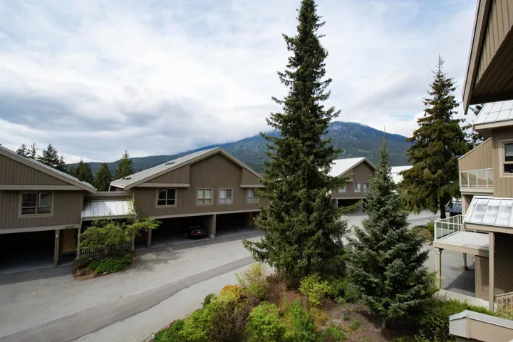 Contemporary multi-level residences featuring covered parking, private balconies with glass railings, and a mountain backdrop