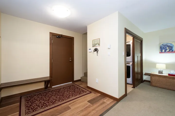 Entryway featuring wood-finish flooring, a built-in wooden bench, and a laundry closet with a stacked washer and dryer