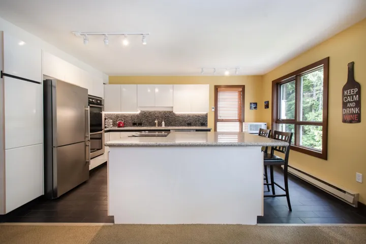 Contemporary kitchen featuring a central island, dark tile flooring, stainless steel appliances, white cabinetry, and a window with wood-finish trim