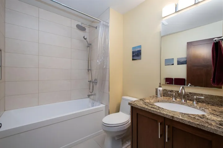 Bathroom featuring a dark wood vanity with a stone countertop and undermount sink, a chrome faucet, a rectangular mirror, and a combination tub and shower with light-toned wall tile