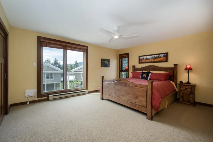 Spacious room featuring light beige carpeting, a large sliding glass door with dark wood trim, and a ceiling fan with integrated lighting