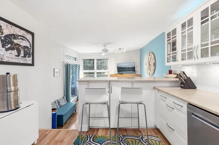 Kitchen featuring white cabinets, glass insert cabinets, a peninsula, light countertops, and stainless steel dishwasher