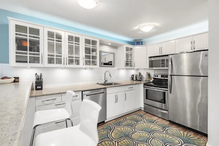 Kitchen featuring appliances with stainless steel finishes, tasteful backsplash, glass insert cabinets, light wood-type flooring, and white cabinetry