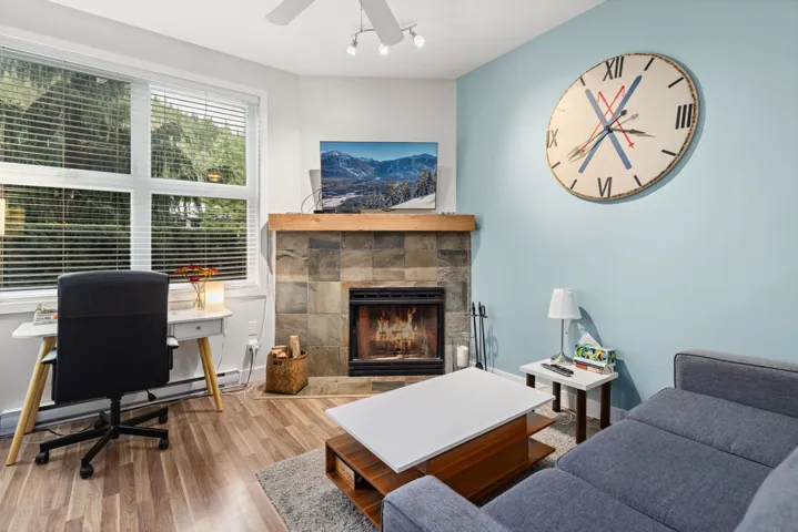 Living room with a fireplace, wood finished floors, baseboard heating, a desk, and ceiling fan
