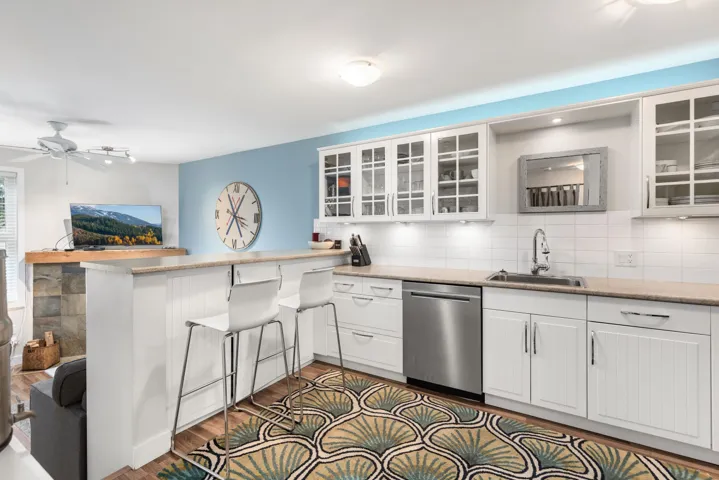 Kitchen featuring white cabinetry, tasteful backsplash, stainless steel dishwasher, a peninsula, and dark wood-style floors