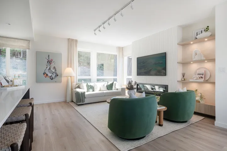 Wood-finish flooring, track lighting, built-in fireplace, recessed shelving with integrated lighting, and a kitchen island with a waterfall countertop
