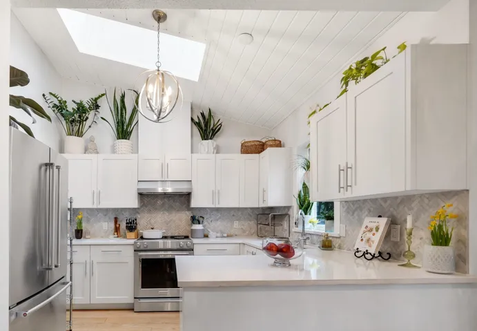 Kitchen with a skylight, high quality appliances, white cabinetry, a peninsula, and decorative backsplash