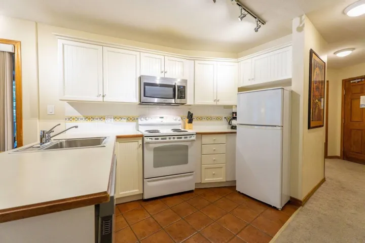 Kitchen featuring white appliances, light countertops, white cabinets, and tasteful backsplash