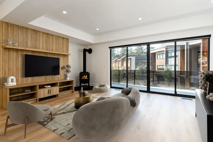 Living area with a wood stove, light wood finished floors, recessed lighting, a tray ceiling, and wooden walls