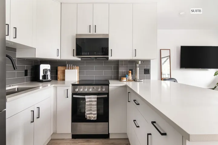 Kitchen with appliances with stainless steel finishes, a peninsula, white cabinetry, tasteful backsplash, and light stone countertops