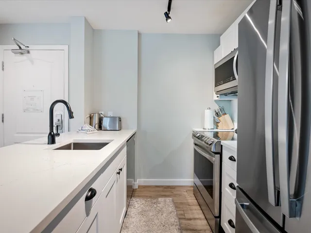 Kitchen with baseboards, light wood-type flooring, white cabinets, appliances with stainless steel finishes, and a sink