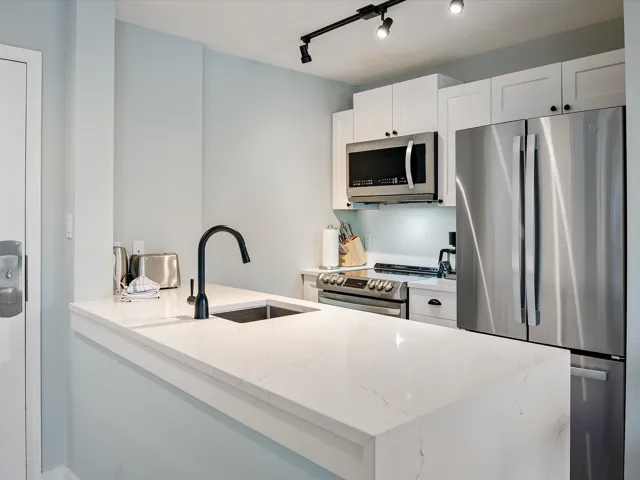 Kitchen with light stone counters, a peninsula, white cabinetry, appliances with stainless steel finishes, and a sink