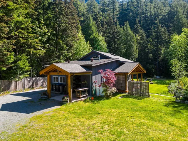 View of front of property featuring a wooded view, fence, a shingled roof, a front yard, and gravel driveway