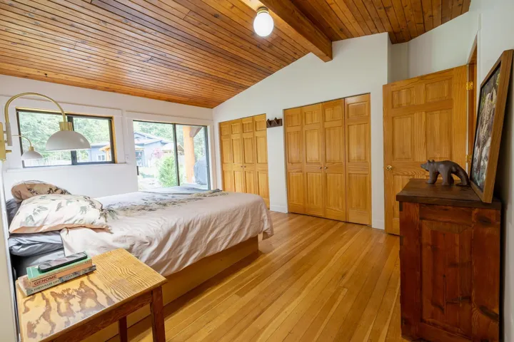 Bedroom with light wood finished floors, vaulted ceiling with beams, two closets, and wood ceiling