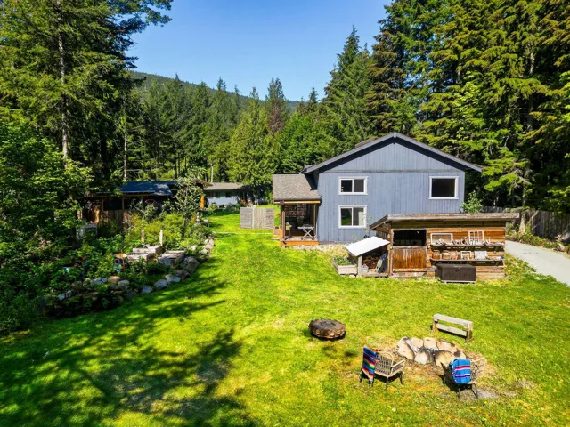 Back of house with central AC unit, a yard, a forest view, and a fire pit
