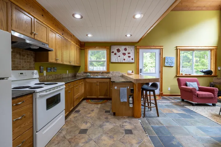 Kitchen featuring under cabinet range hood, white appliances, a kitchen bar, and recessed lighting