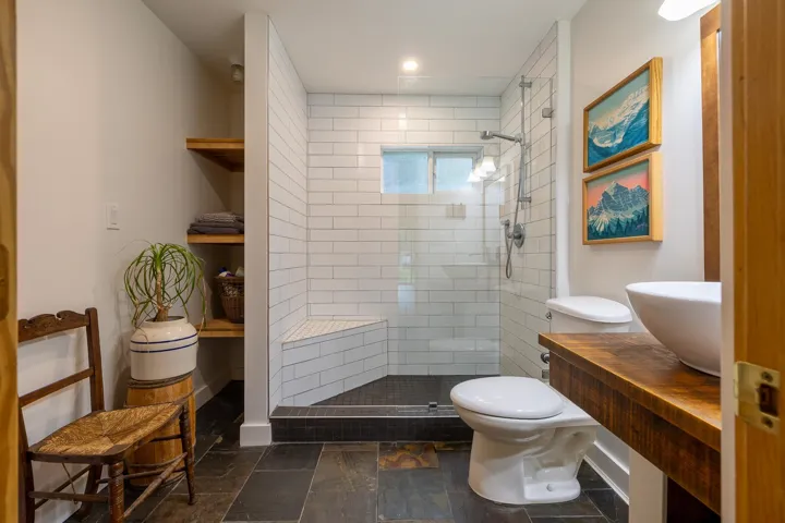 Full bathroom featuring toilet, tiled shower, stone finish flooring, and a sink