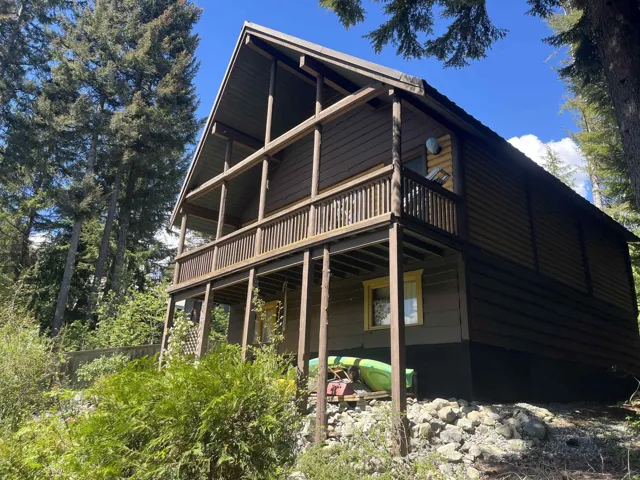Two-story rustic cabin featuring a gabled roofline, wooden siding, and a full-length second-story balcony with wood railings