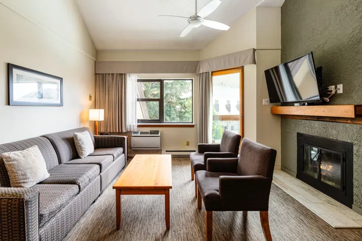 Living area featuring lofted ceiling, a fireplace with flush hearth, a ceiling fan, and a baseboard heating unit