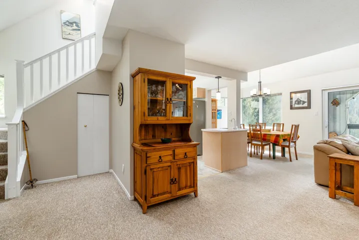 Open-concept living area featuring light-colored carpeting, a staircase with white balusters, and a kitchen island with a sink