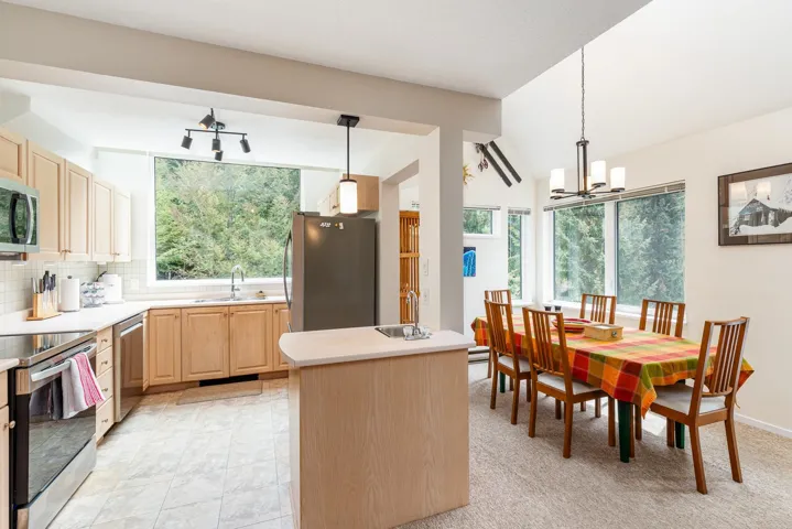 Kitchen and dining area featuring light wood cabinetry, stainless steel appliances, a kitchen island with a sink, and a dining space with large windows