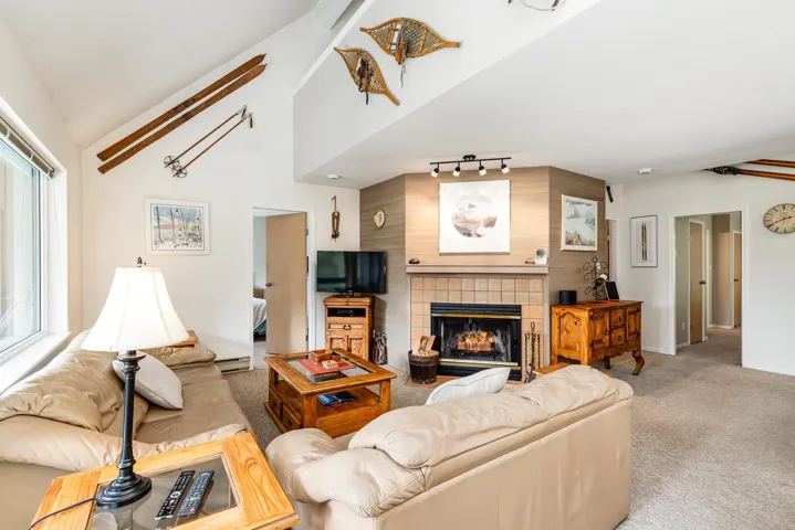 Living area featuring vaulted ceilings, a large window, a tiled fireplace with hearth, track lighting, and soft carpeting