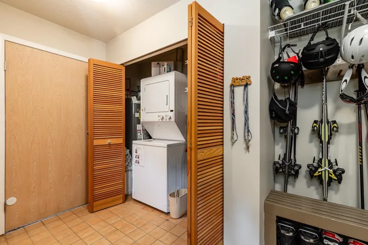 Compact laundry area featuring a stacked washer and dryer unit, louvered bi-fold doors, and a neutral tile floor