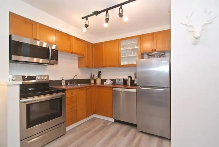 Kitchen with appliances with stainless steel finishes, glass insert cabinets, dark countertops, light wood-type flooring, and brown cabinets