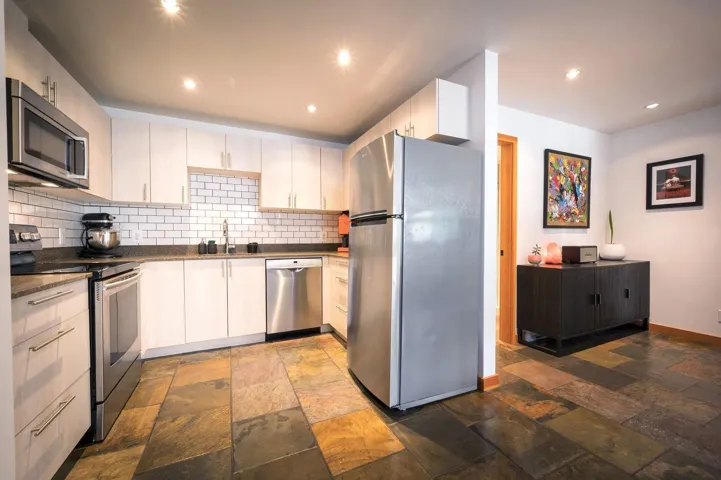 Kitchen featuring appliances with stainless steel finishes, backsplash, recessed lighting, stone tile floors, and dark stone counters