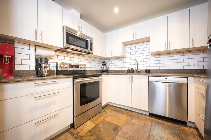 Kitchen featuring stainless steel appliances, dark stone counters, stone tile flooring, and tasteful backsplash