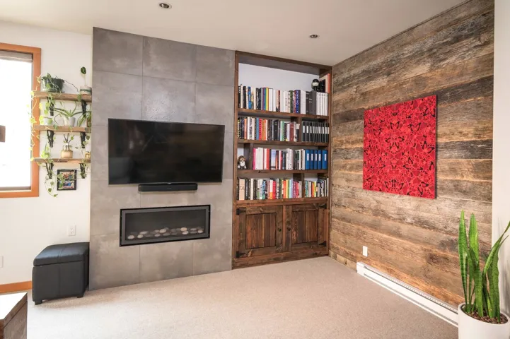 Carpeted living room featuring a baseboard heating unit, a tile fireplace, and wood walls