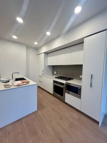 Kitchen featuring modern cabinets, light countertops, white cabinets, stainless steel appliances, and light wood-style flooring