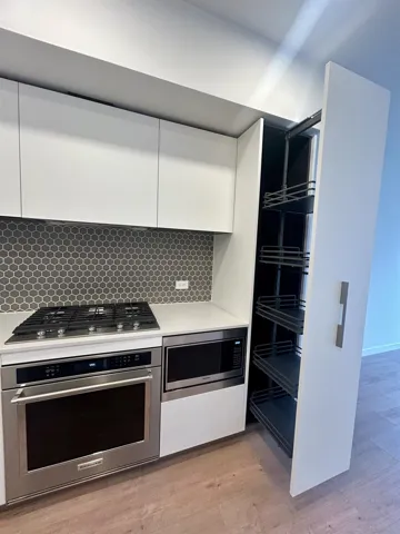 Kitchen with stainless steel appliances, white cabinetry, backsplash, light wood-type flooring, and modern cabinets