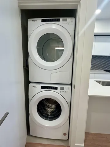 Washroom with estacked washer and dryer and wood finished floors