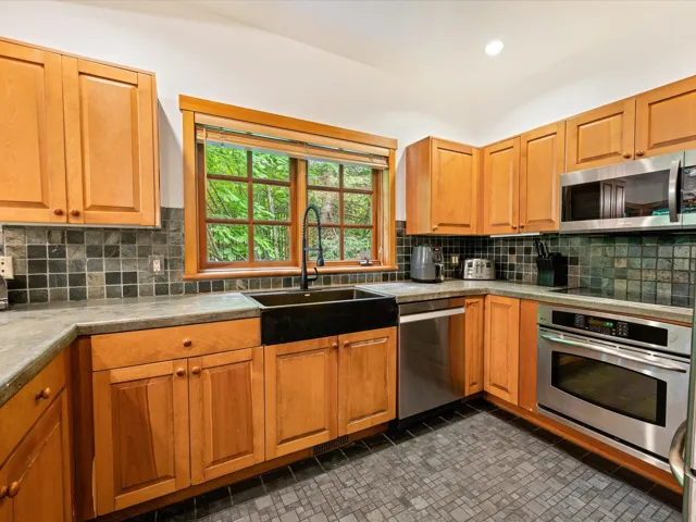 Kitchen with stainless steel appliances, backsplash, light countertops, and brown cabinetry