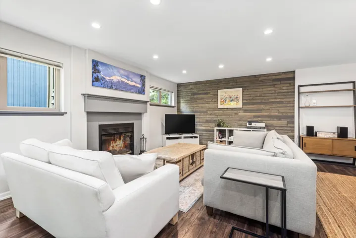 Living room with a glass covered fireplace, recessed lighting, wood walls, an accent wall, and dark wood-style flooring