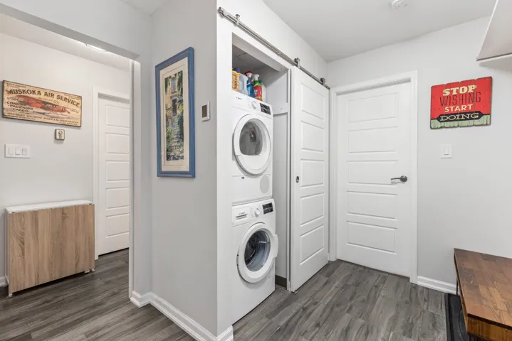 Clothes washing area featuring stacked washing machine and dryer, dark wood-style floors, a barn door, and baseboards