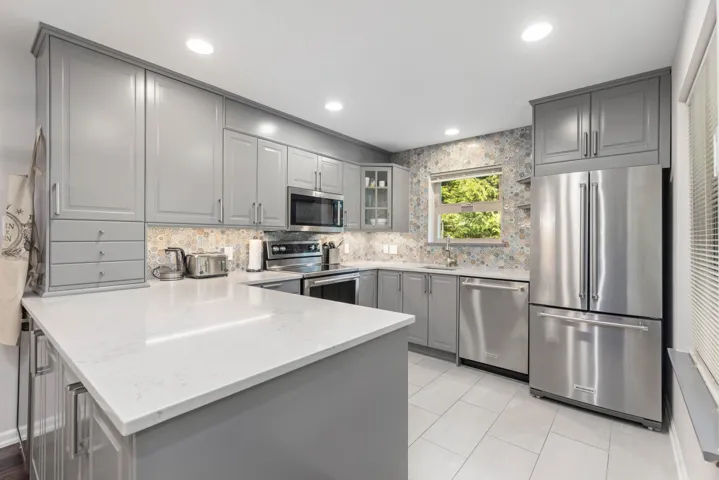 Kitchen with appliances with stainless steel finishes, gray cabinetry, a peninsula, a sink, and decorative backsplash