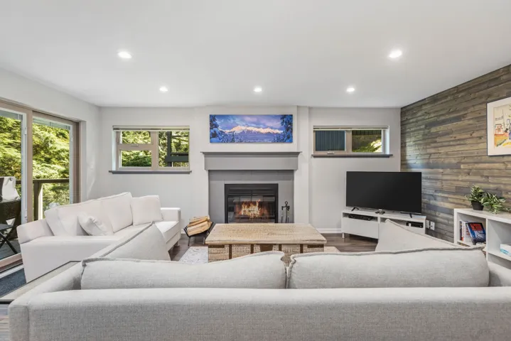 Living room featuring wooden walls, recessed lighting, a glass covered fireplace, wood finished floors, and an accent wall