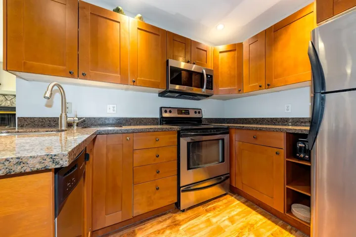 Kitchen with stainless steel appliances, light wood finished floors, a sink, brown cabinetry, and recessed lighting