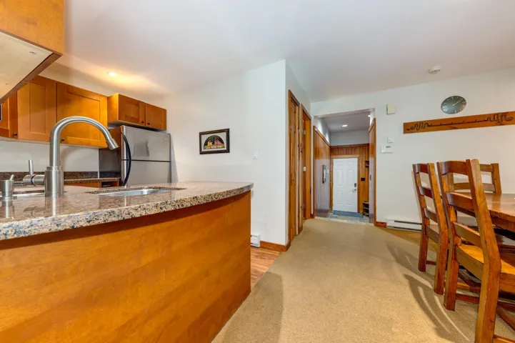 Kitchen with brown cabinetry, baseboard heating, freestanding refrigerator, recessed lighting, and light stone counters