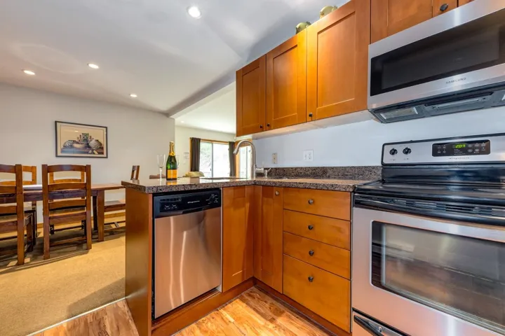 Kitchen featuring appliances with stainless steel finishes, light wood-style floors, a peninsula, brown cabinetry, and dark countertops