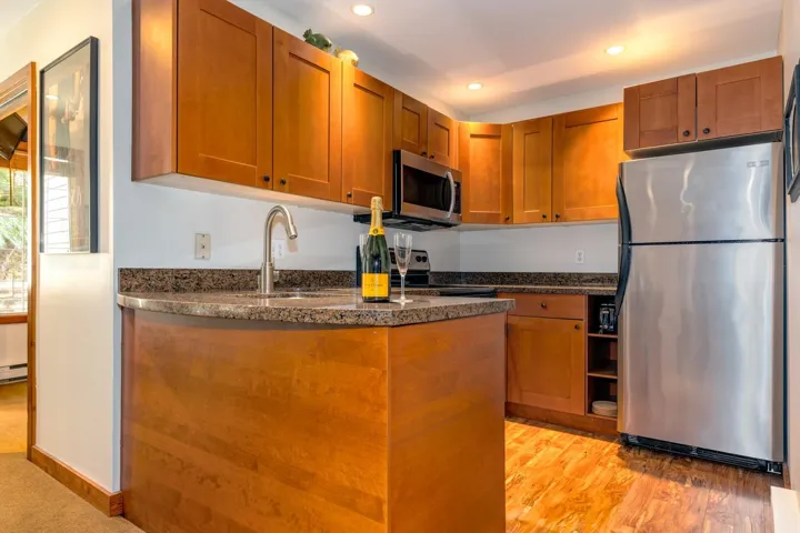 Kitchen featuring stainless steel appliances, brown cabinets, recessed lighting, dark stone counters, and a peninsula
