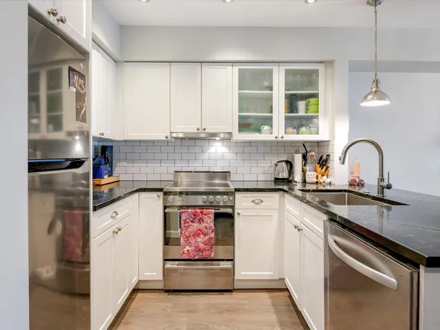 Kitchen with under cabinet range hood, a sink, appliances with stainless steel finishes, light wood-type flooring, and tasteful backsplash