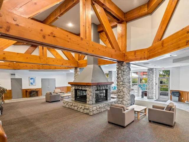 Carpeted living area featuring beam ceiling, a wainscoted wall, a fireplace, decorative columns, and high vaulted ceiling